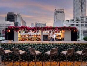 A rooftop bar with a city skyline view, a bar counter with bottles, and seating with a patterned backdrop. - Novotel Bangkok Platinum Pratunam (Bangkok)
