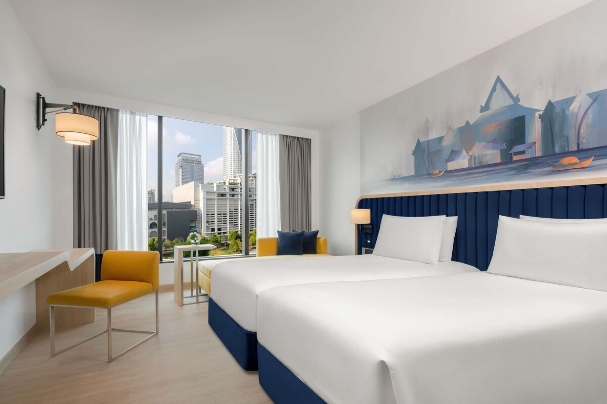 A hotel room with a large bed, a desk, a chair, and a city view.
