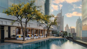 A modern hotel with a pool, outdoor seating, and a view of the city skyline.