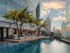 A modern hotel with a pool, outdoor seating, and a view of the city skyline. - Novotel Bangkok Platinum Pratunam (Bangkok)