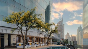 Um hotel moderno com piscina, área externa para sentar e vista para o horizonte da cidade.
