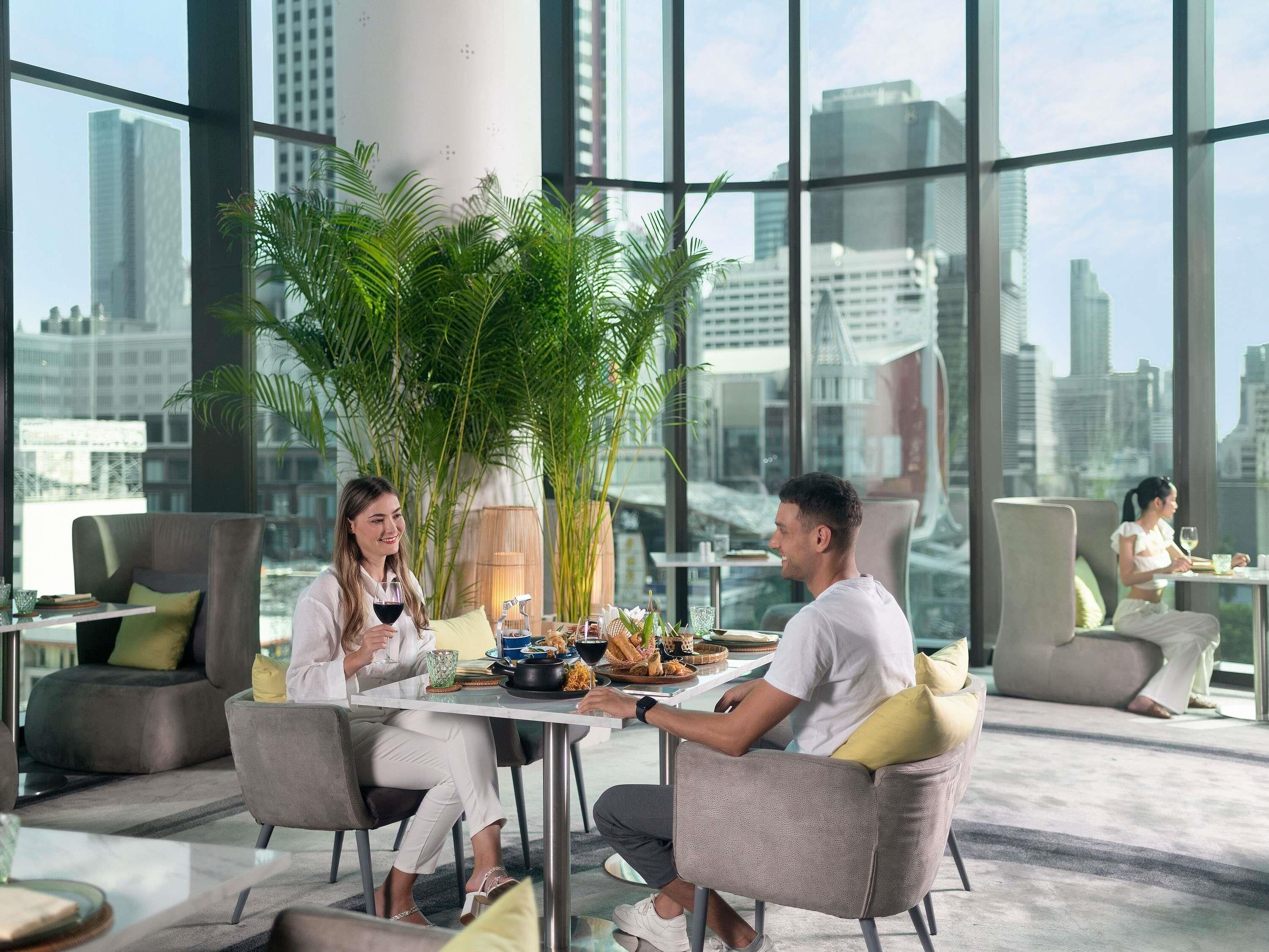 A modern dining area with large windows, a central plant, and a city view.