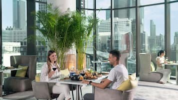 A modern dining area with large windows, a central plant, and a city view.