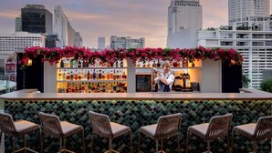 Um bar no terraço com vista para o horizonte da cidade, balcão de bar com garrafas e assentos com fundo estampado.