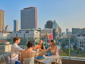 A group of people dining at a table with a cityscape view, including tall buildings and a clear sky. - Novotel Bangkok Platinum Pratunam (Bangkok)