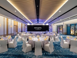 A conference room with round tables, white chairs, and a large screen displaying 'NOVOTEL BANGKOK PLATINUM PRATUMAN'. - Novotel Bangkok Platinum Pratunam (Bangkok)