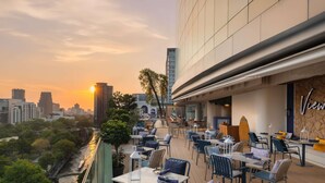 Área de refeições ao ar livre com mesas e cadeiras, com vista para um horizonte urbano e um rio.