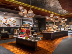 A modern restaurant interior with a central dining area, multiple hanging light fixtures, and a colorful wall mural. - Novotel Bangkok Platinum Pratunam (Bangkok)