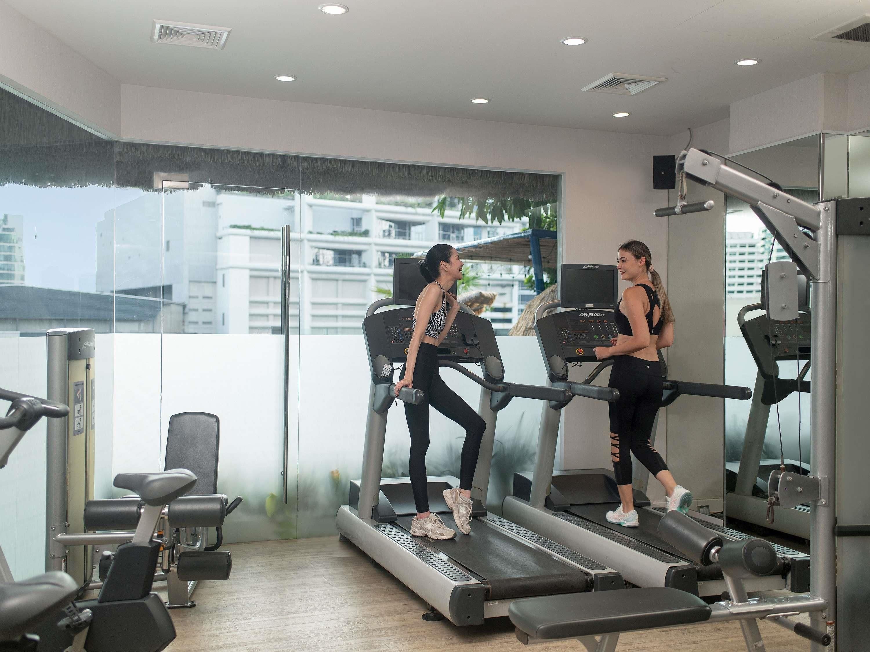 Un gimnasio con cintas de correr, máquinas de pesas y un amplio ventanal con vistas a edificios.