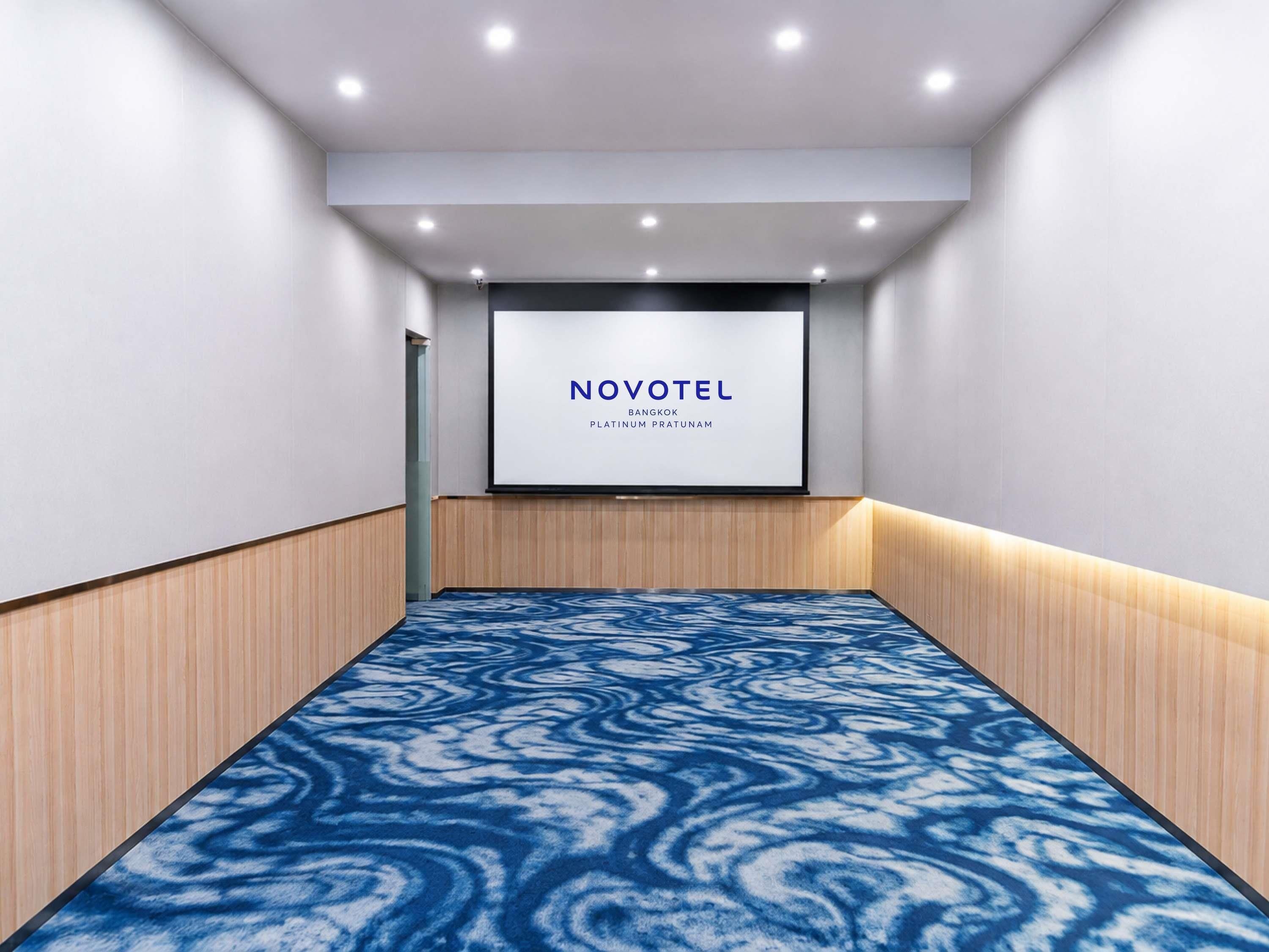 A conference room with a large screen displaying 'NOVOTEL' and 'BANGKOK PLATINUM PRATUNAM' text.