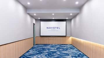 A conference room with a large screen displaying 'NOVOTEL' and 'BANGKOK PLATINUM PRATUNAM' text.