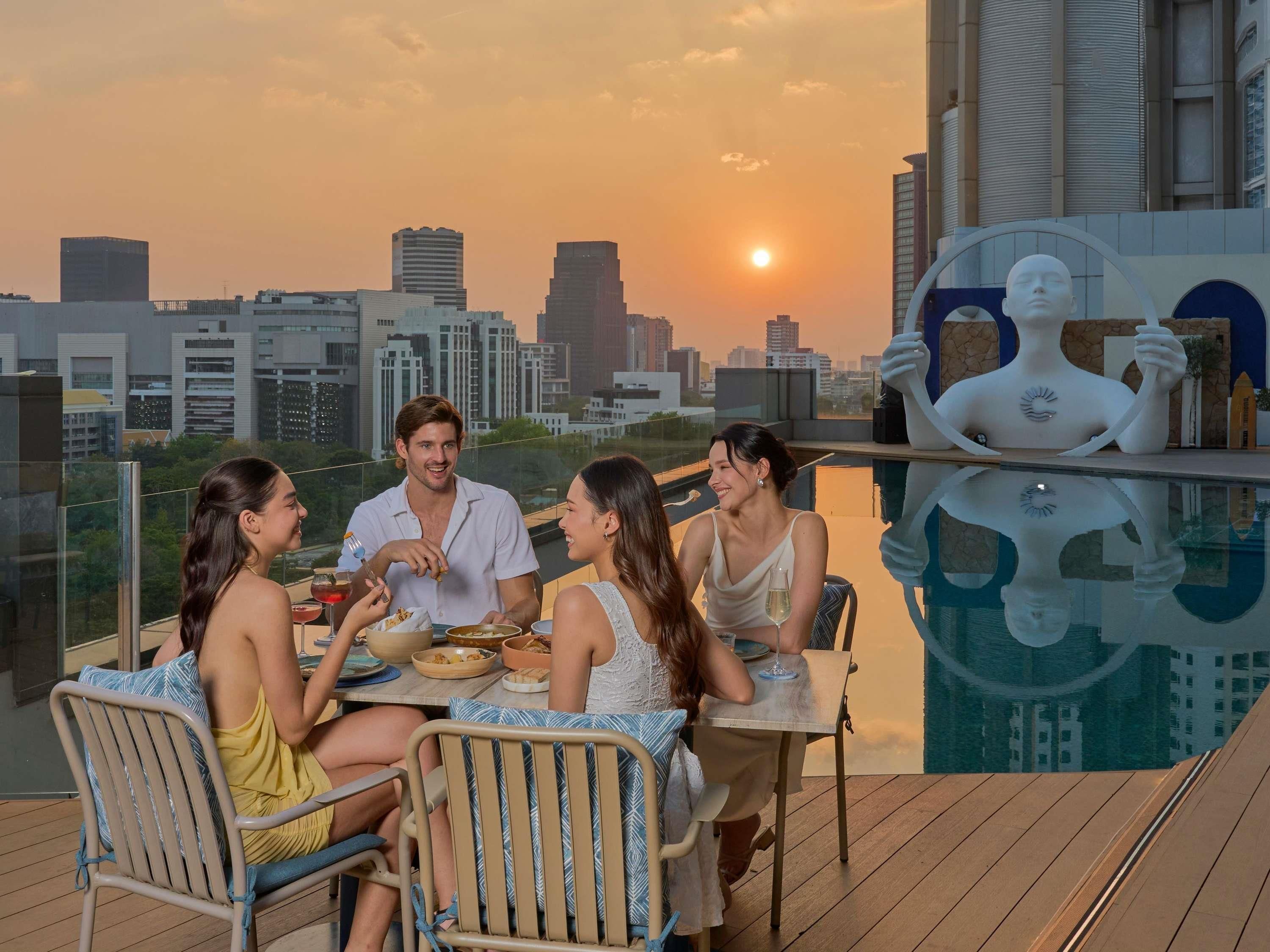Un área de comedor en la azotea con vista a la ciudad, una piscina y una estatua.