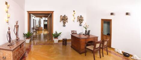 A spacious hallway with a wooden desk, chairs, and decorative items like statues and wall sconces.