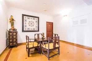 A dining area with a wooden table and chairs, a decorative cabinet, a framed floral artwork, and a wooden door. - Tissa's Inn (Kochi)