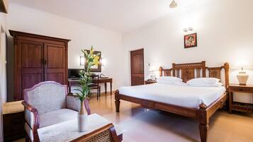 Um quarto com uma cama de madeira grande, um guarda-roupa de madeira, uma escrivaninha com cadeira e uma mesa de cabeceira com abajur.