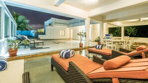 A spacious outdoor lounge area with wicker furniture and orange cushions, a dining area with white chairs, and potted plants. - Tissa's Inn (Kochi)