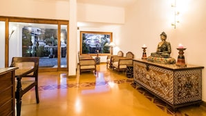 A room with a wooden floor, a large window, a Buddha statue, and a patterned cabinet. - Tissa's Inn (Kochi)