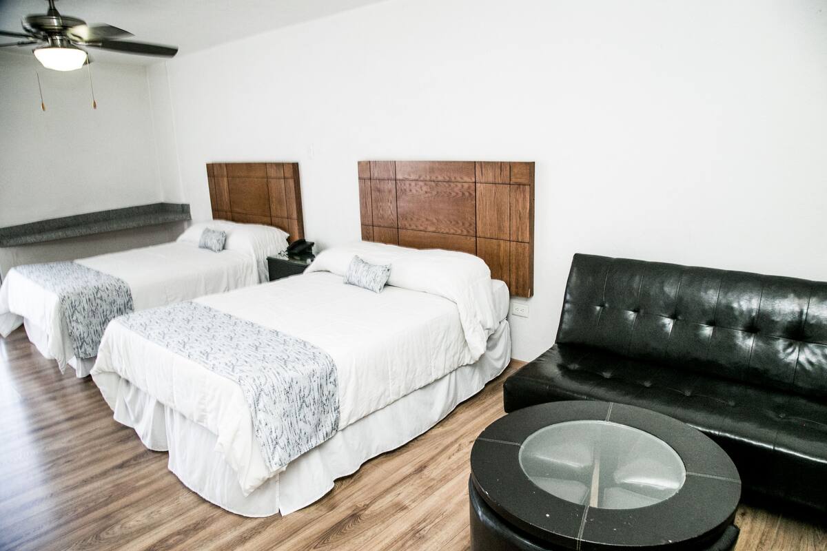 A hotel room with two beds, a black leather sofa, and a round coffee table.
