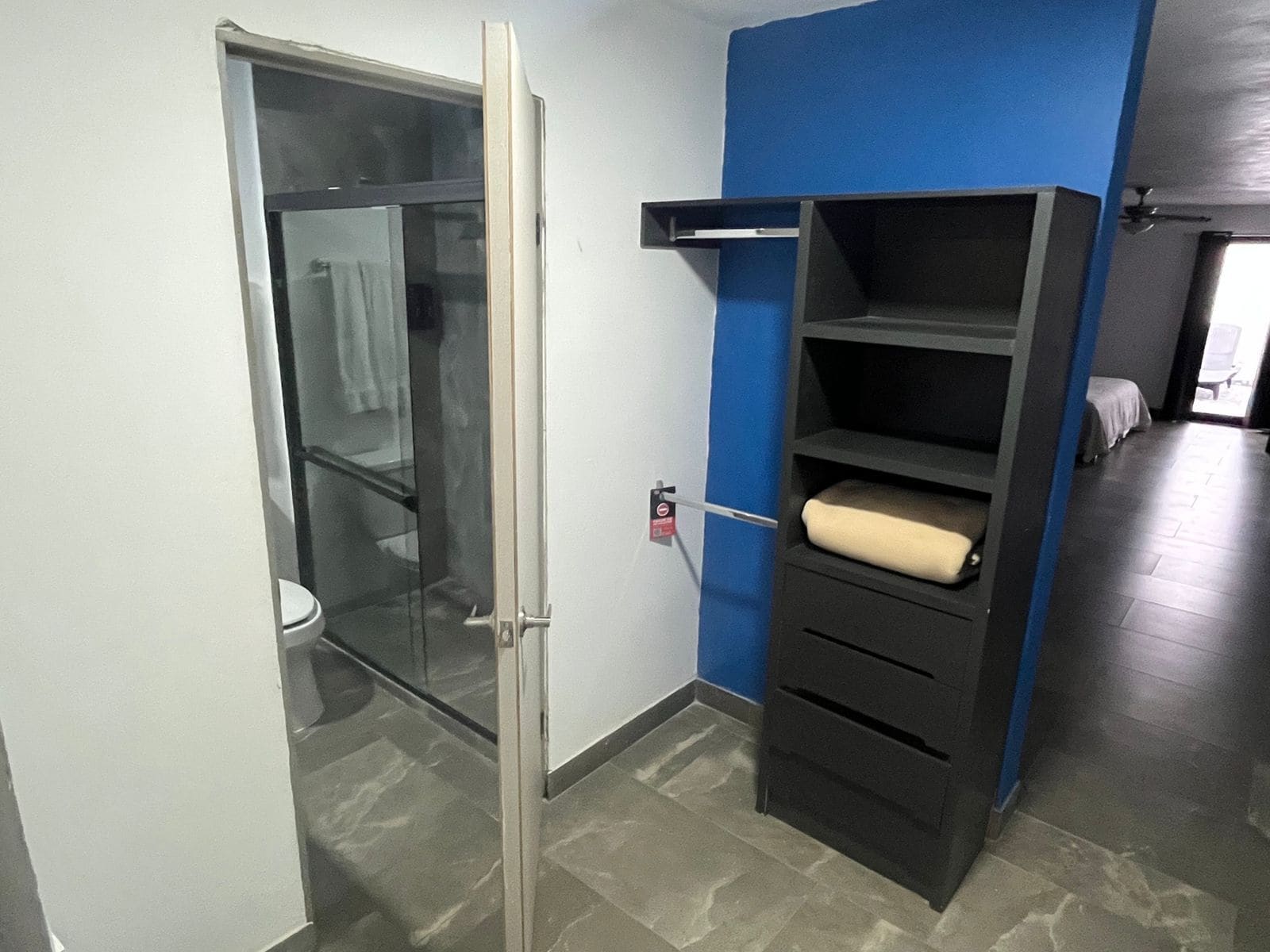 Ein Badezimmer mit Duschkabine aus Glas, Toilette, blauer Wand und schwarzem Stauraum mit Schubladen und Regalen.