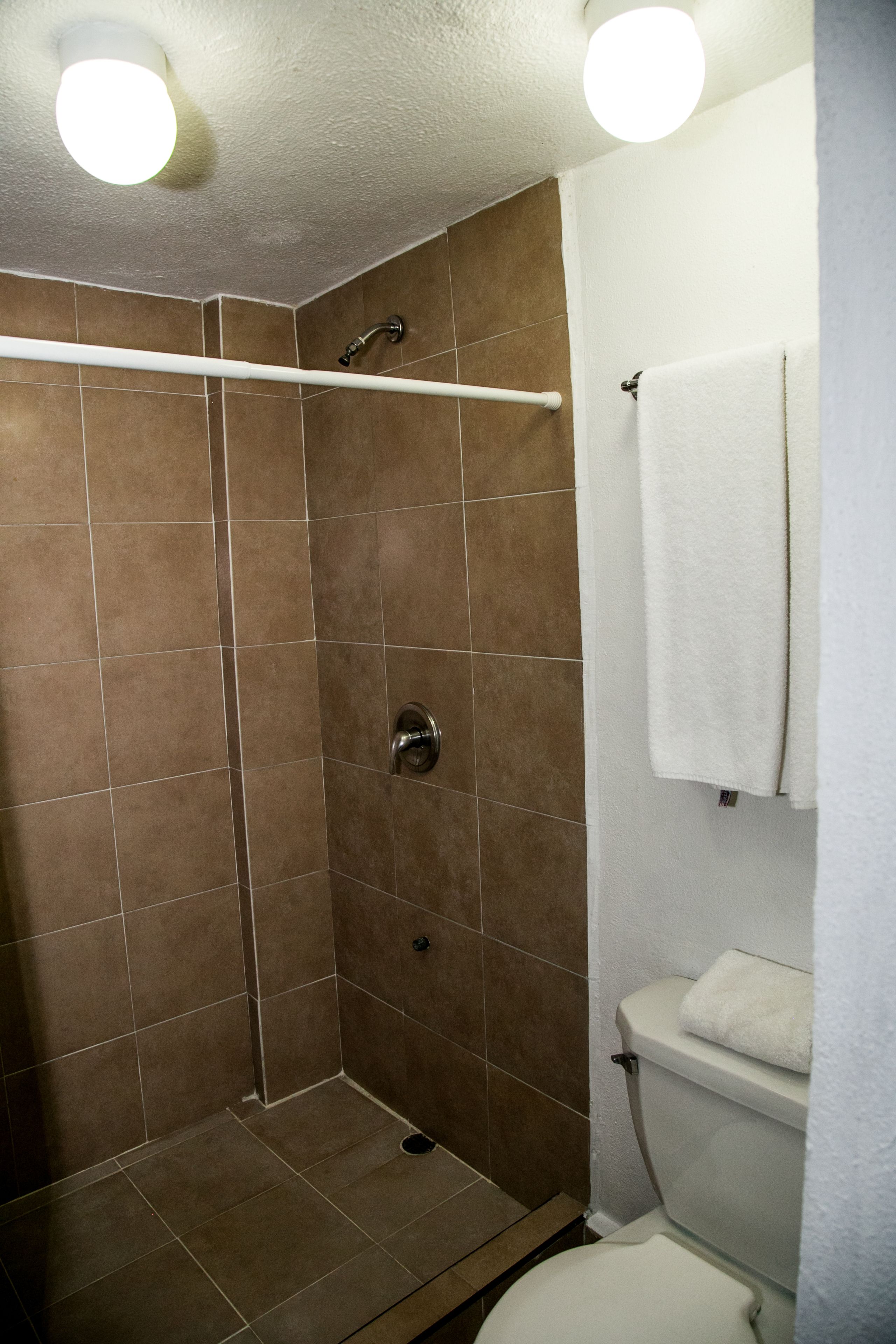 A shower with brown tiles, a white towel, and a glass-enclosed toilet.