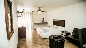 A hotel room with a bed, a desk, a chair, a ceiling fan, and a small table. - Suites DIOH (Monterrey)