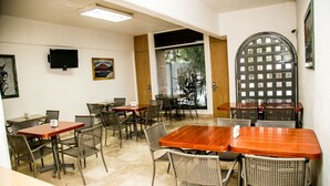 A dining area with multiple tables and chairs, a television mounted on the wall, and a large arched door. - Suites DIOH (Monterrey)