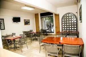 A dining area with multiple tables and chairs, a television mounted on the wall, and a large arched door.