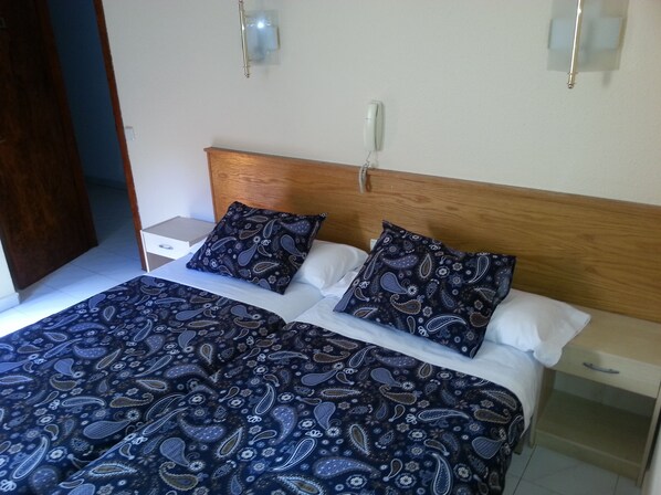 Una cama doble con cabecera de madera, dos mesitas de noche y una colcha estampada.