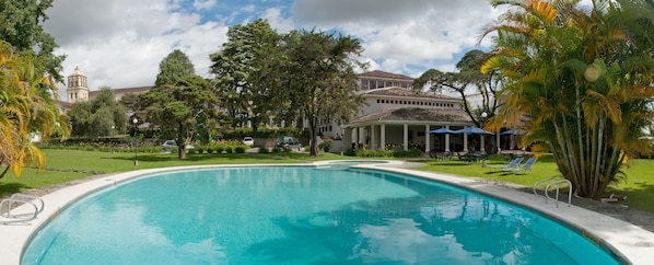 A swimming pool with a clear blue water, surrounded by lush greenery and a building with a dome in the background. - Dann Monasterio Popayan (Popayán)