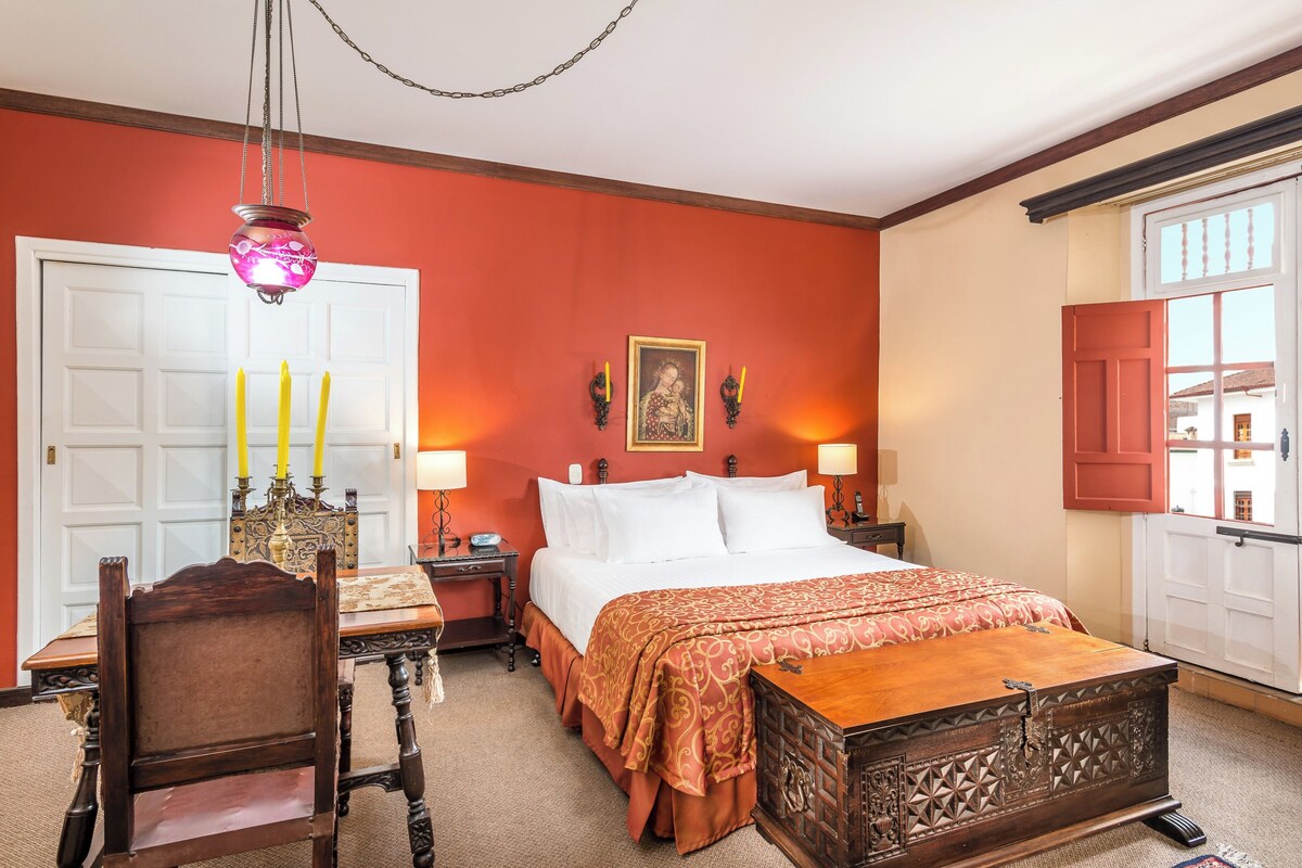 A bedroom with a bed, bedside tables, a wooden chair, a chest of drawers, and a chandelier.