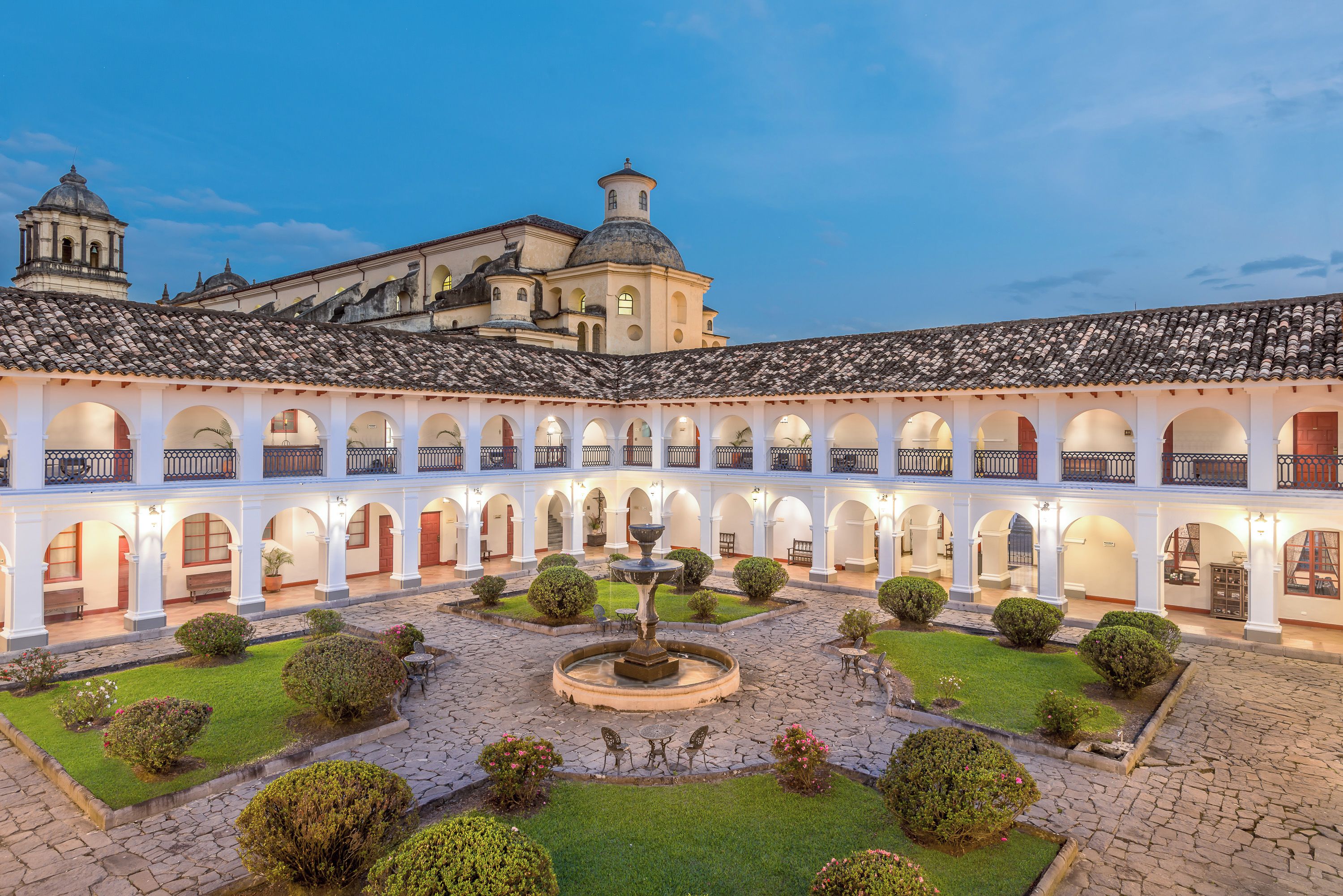 A courtyard with a fountain, surrounded by arches and greenery, leading to a building with domed architecture.