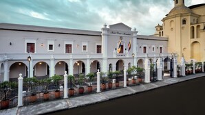 A historic building with a central archway, flags, and a fountain. - Hotel Dann Monasterio Popayán (Popayán)