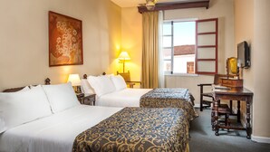 A hotel room with two beds, a desk, a lamp, a painting, and a window with a view. - Hotel Dann Monasterio Popayán (Popayán)