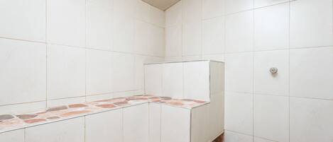 A bathroom with white tiles and a shower area.