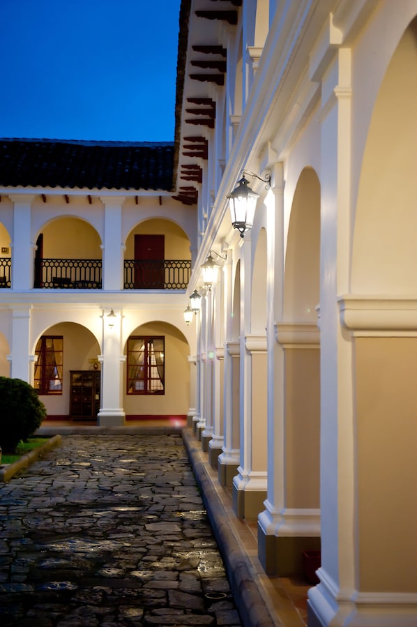 A courtyard with a cobblestone path, white columns, and arched doorways. - Dann Monasterio Popayan (Popayán)