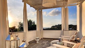 A balcony with a view of the sea, white furniture, and a hanging light fixture. - La Suite Boutique Hotel (Procida)