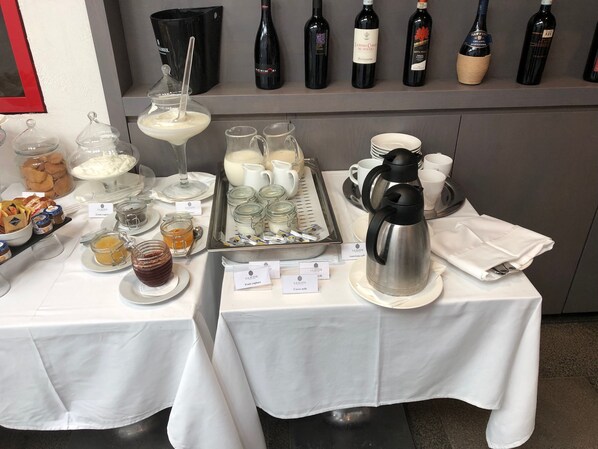 Um buffet de café da manhã com diversas opções de comida, um canto para café e uma seleção de garrafas de vinho à mostra.