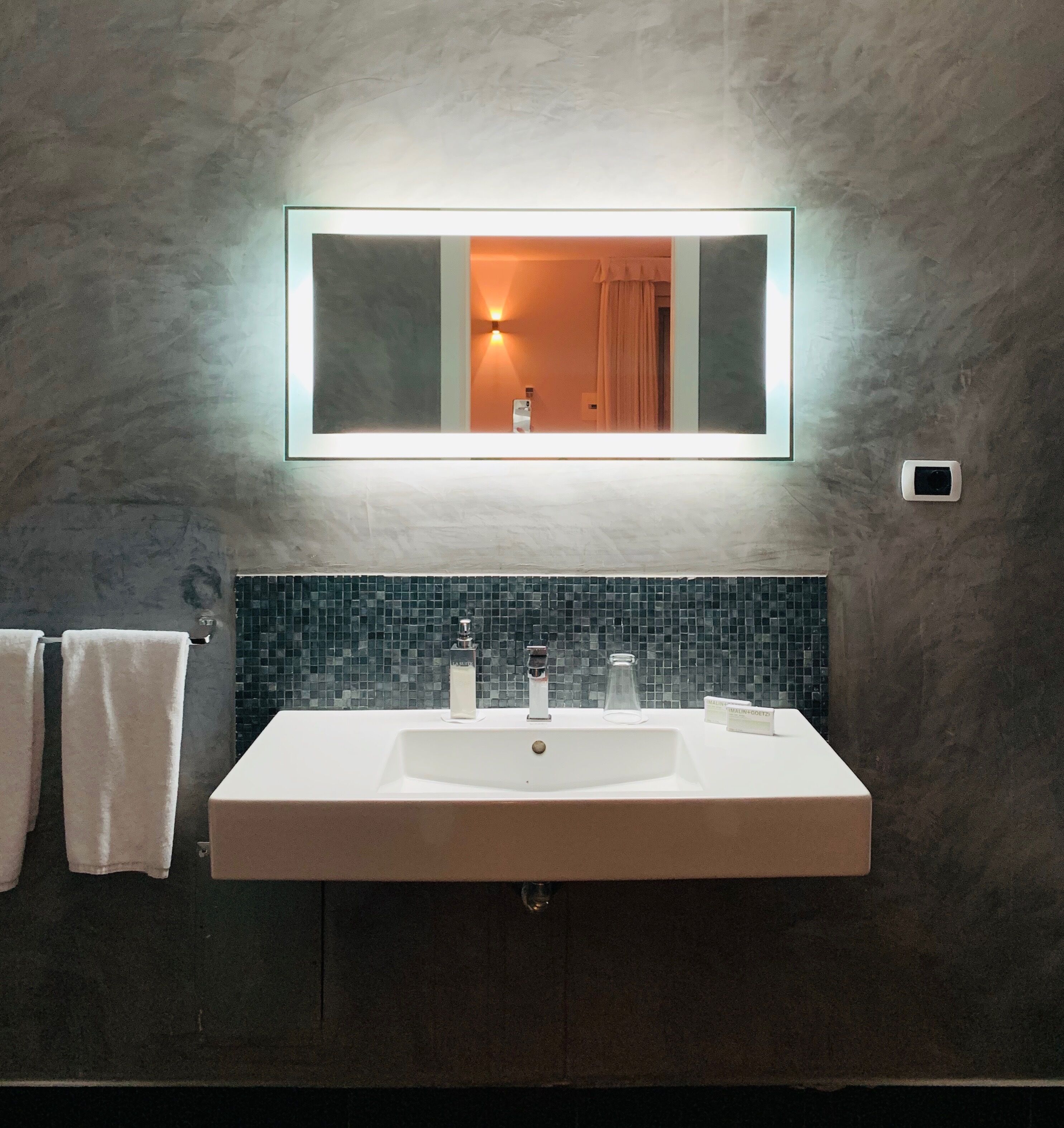 Un baño con un lavamanos grande y rectangular, un espejo encima y un salpicadero de azulejos.