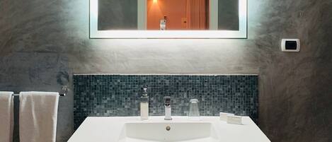 Un baño con un lavamanos grande y rectangular, un espejo encima y un salpicadero de azulejos.