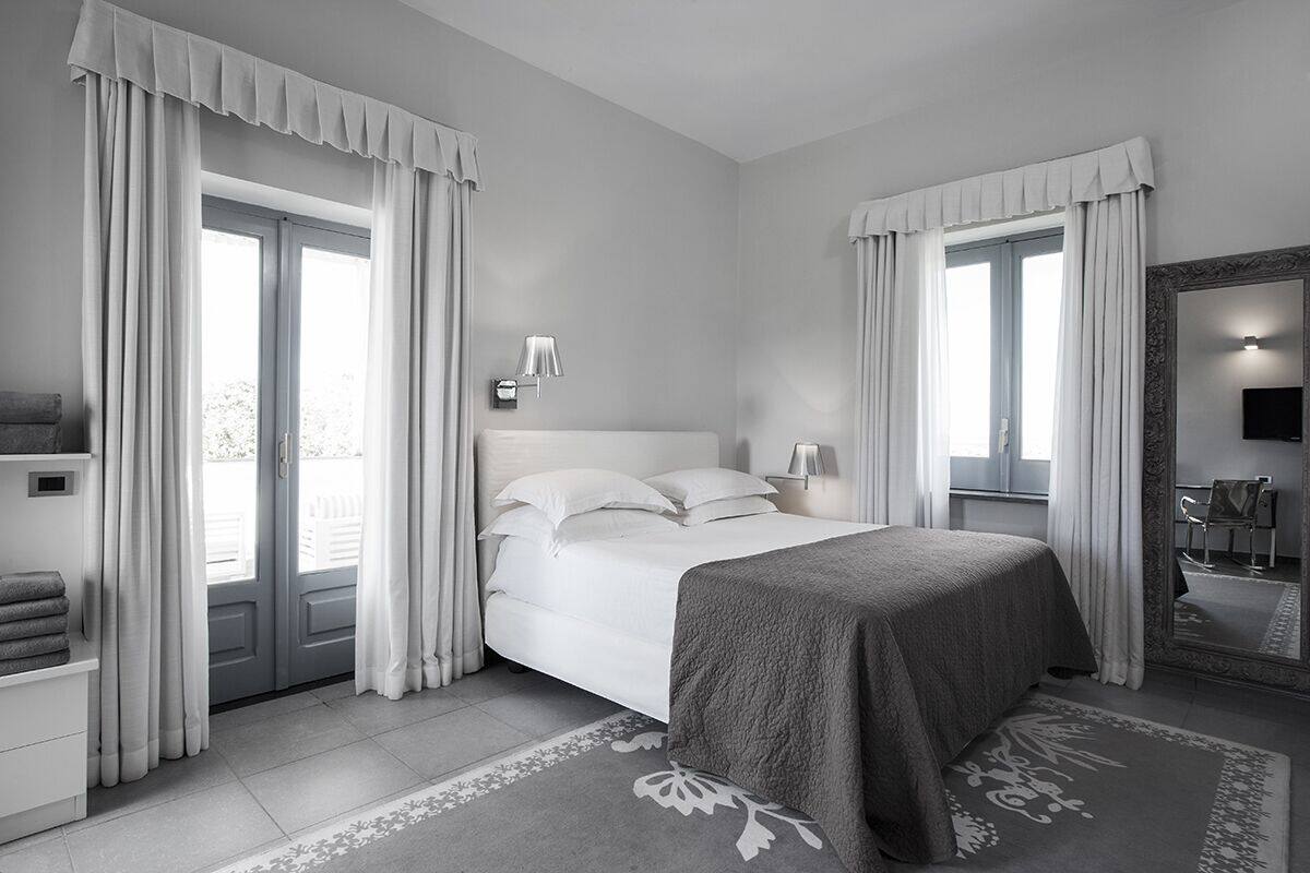 A modern bedroom with a bed, curtains, a mirror, and a nightstand.