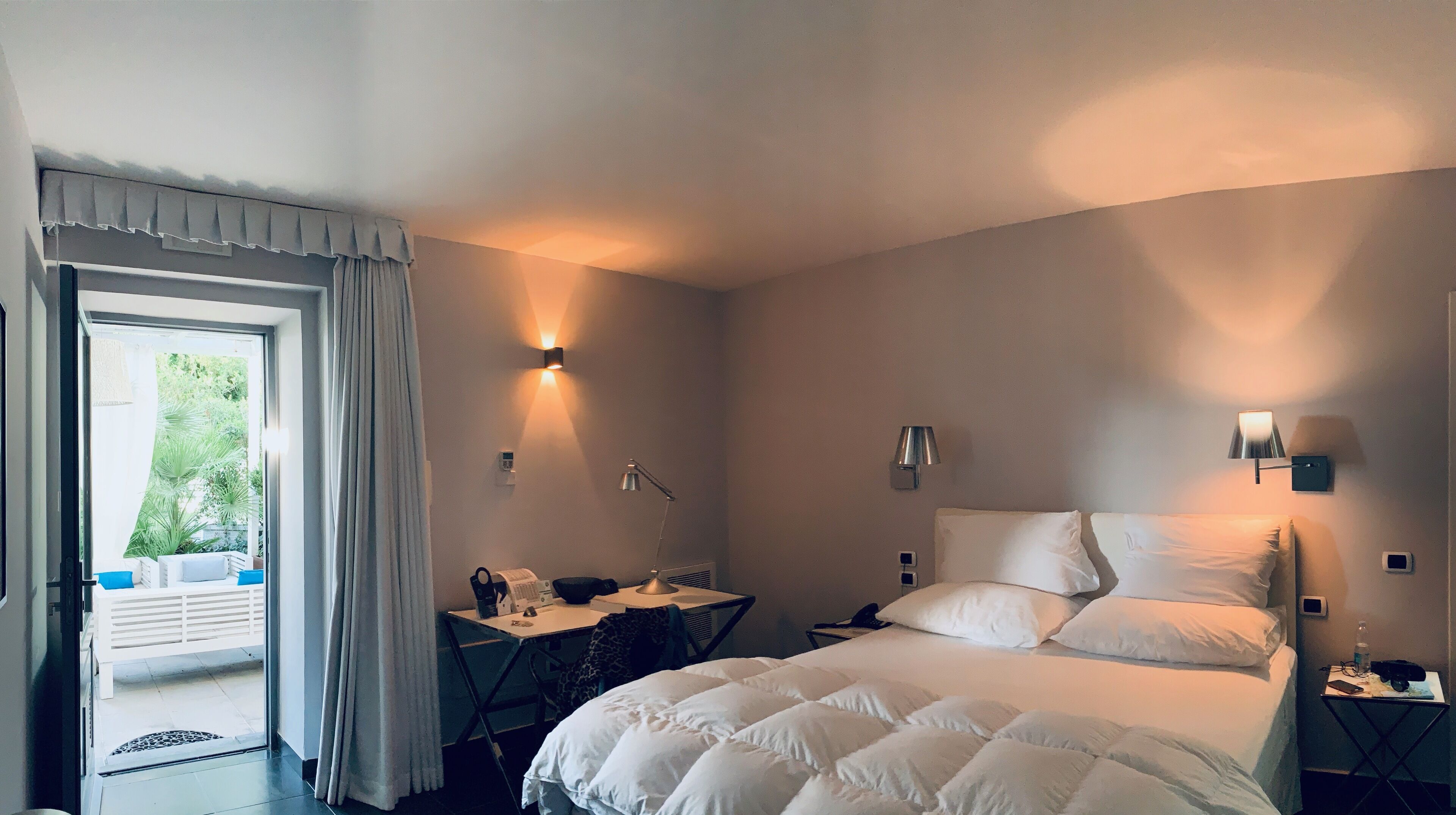 Una habitación de hotel con cama, escritorio, silla, computadora y ventana con cortinas.