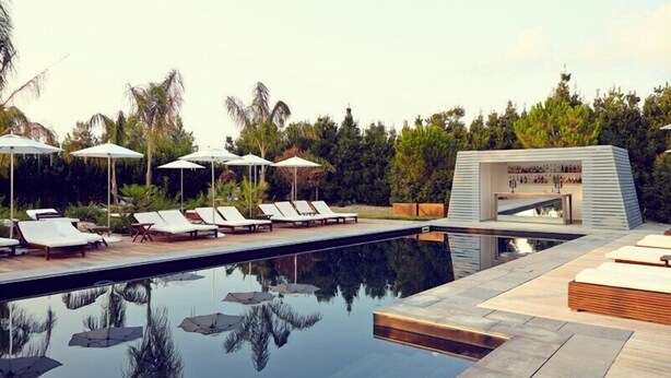 A modern pool area with lounge chairs and umbrellas, surrounded by lush greenery. - La Suite Boutique Hotel (Procida)