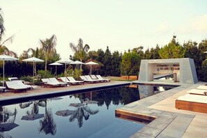 Uma área de piscina moderna com espreguiçadeiras e guarda-sóis, cercada por vegetação exuberante.
