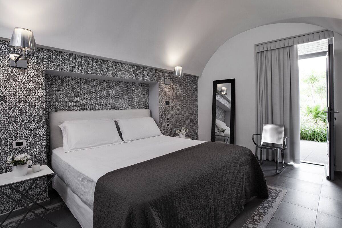 A modern hotel room with a large bed, a bedside table with a lamp, a chair, and a view of greenery outside.