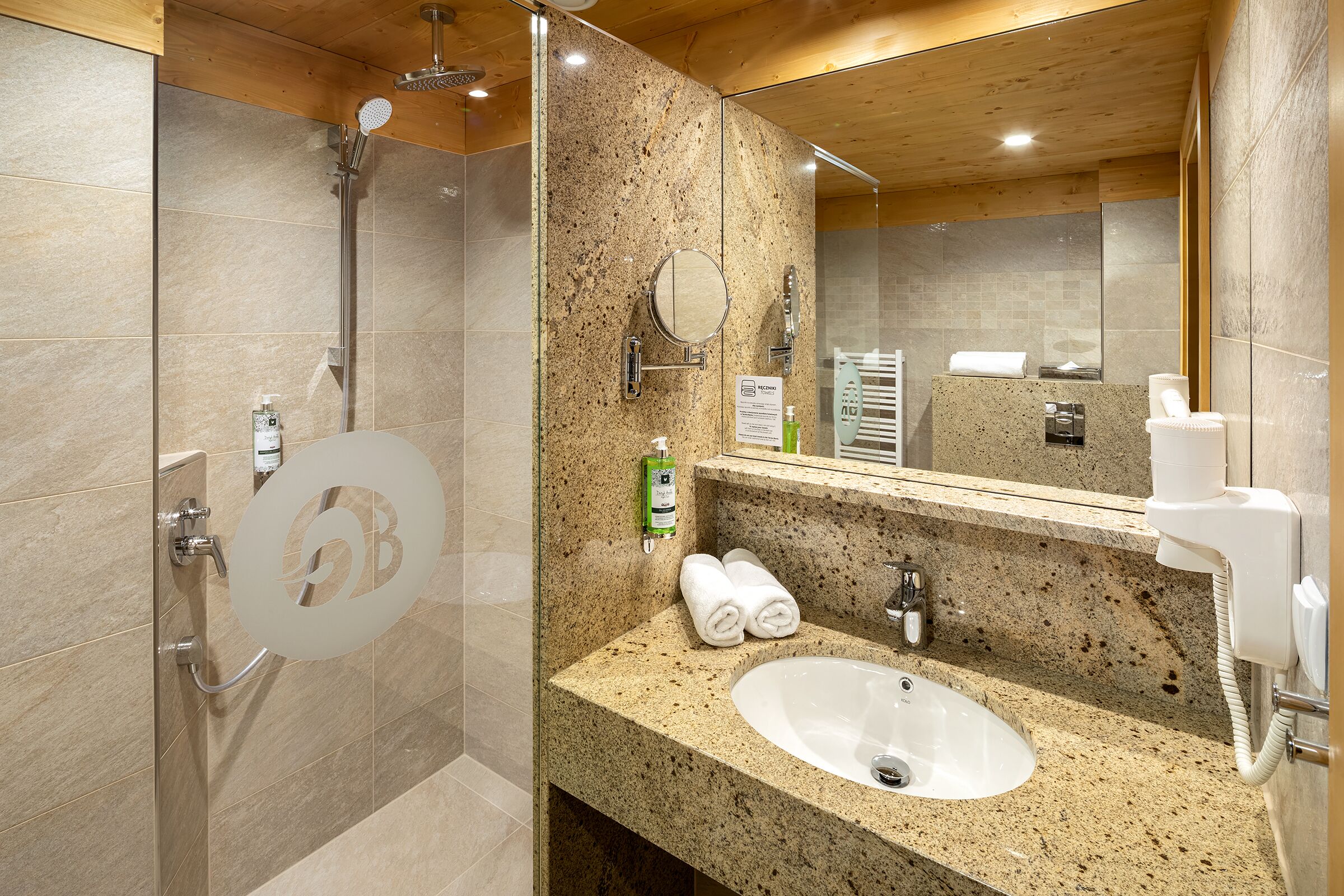 A modern bathroom with a granite countertop sink, a glass shower enclosure, and a wooden ceiling.