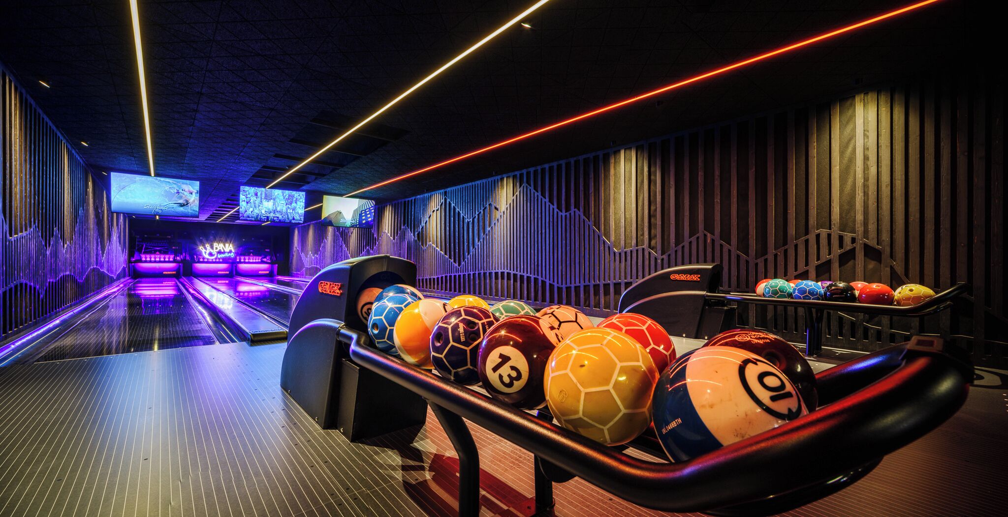 A bowling alley with multiple lanes, a bowling ball rack, and a neon-lit ceiling.