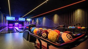 A bowling alley with multiple lanes, a bowling ball rack, and a neon-lit ceiling.
