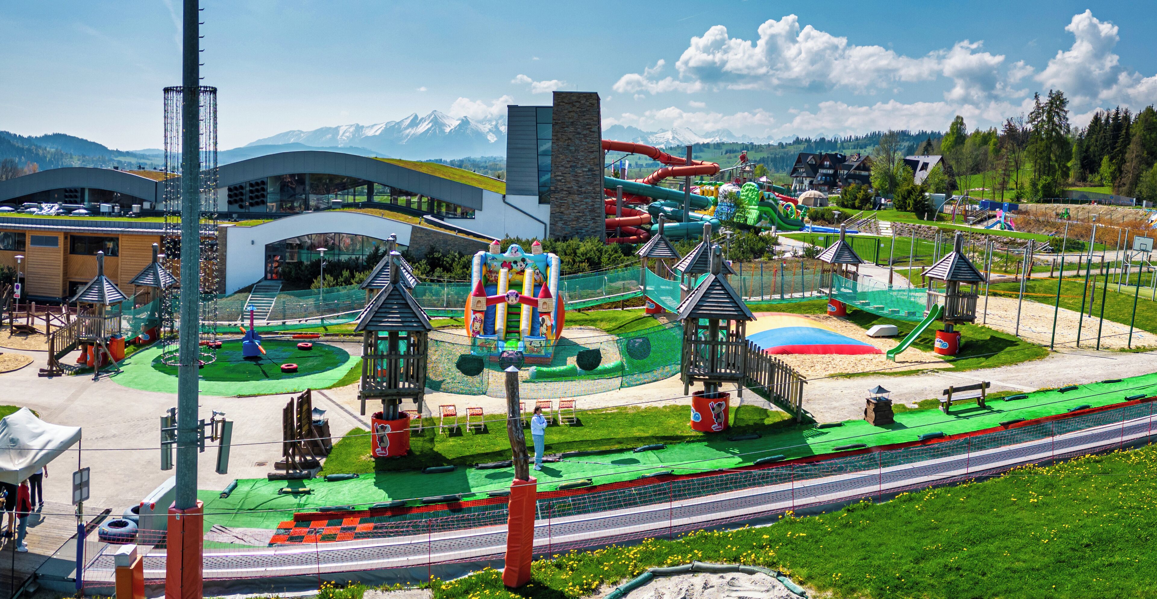 A modern building with a curved roof and a playground area with slides and climbing structures.