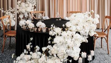 A table set for a formal event with white flowers and candles, wooden chairs, and a black tablecloth.