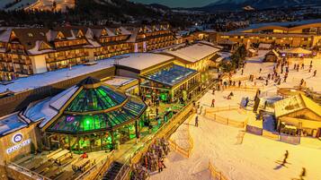 A ski resort with multiple buildings, including a restaurant named "Bania Ski" with outdoor seating and a glass-roofed structure.